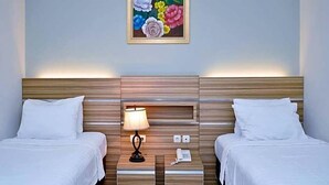 Habitación de hotel con dos camas, una mesita de noche con lámpara, teléfono y un cuadro en la pared.