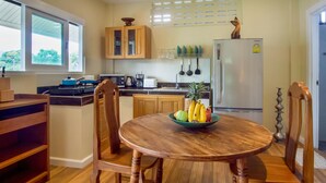 Una cocina con armarios de madera, un refrigerador, una mesa de comedor con sillas y un frutero.