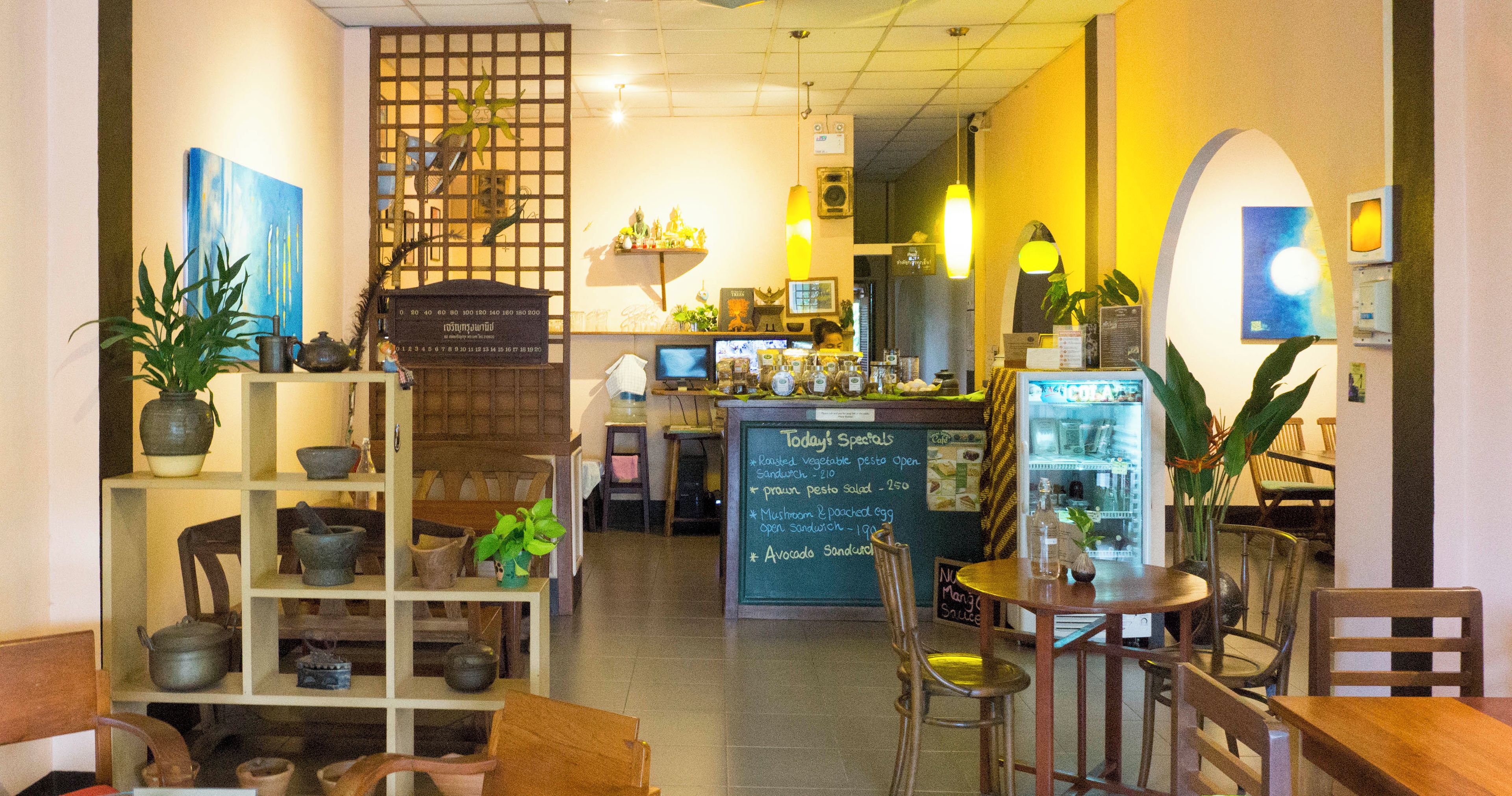 A café interior with wooden furniture, a menu board, and various plants.