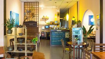 A café interior with wooden furniture, a menu board, and various plants.