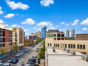 Un paisaje urbano con cielo despejado, una mezcla de edificios modernos y antiguos, y una calle bordeada de coches aparcados.