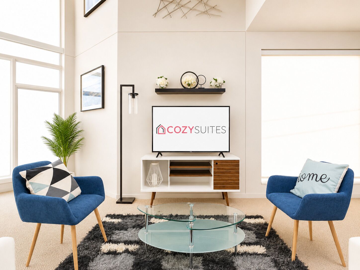A modern living room with a flat-screen TV, two blue armchairs, a glass coffee table, and a black and white rug.
