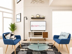 Un salon moderne avec un téléviseur à écran plat, deux fauteuils bleus, une table basse en verre et un tapis noir et blanc.