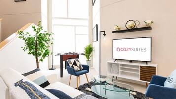 Una sala de estar moderna con sofá, una mesita de centro y un televisor mostrando 'COZY SUITES'.