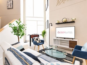 Ein modernes Wohnzimmer mit einer Couch, einem Couchtisch und einem Fernseher, der 'COZY SUITES' zeigt.