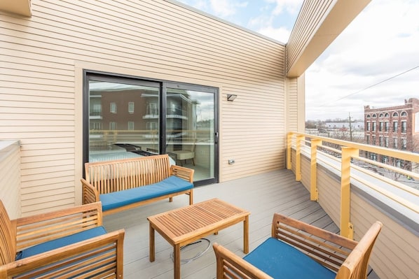 Un balcón con muebles de madera, una puerta de cristal y vistas a edificios.
