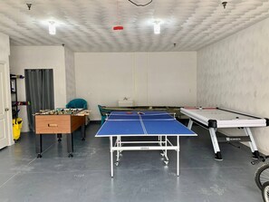 A room with a ping pong table, a foosball table, and a table tennis table.