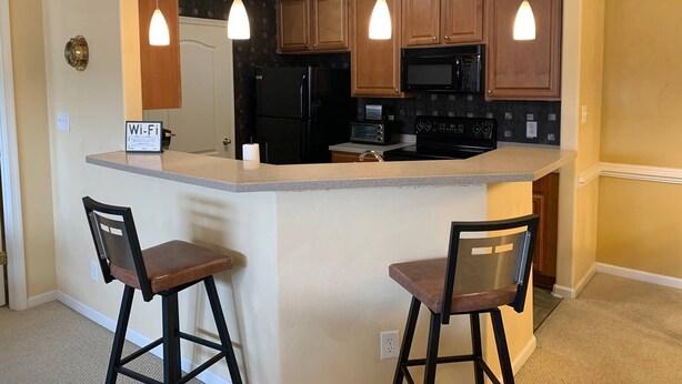 A kitchen with wooden cabinets, a black refrigerator, a microwave, a stove, and two bar stools.