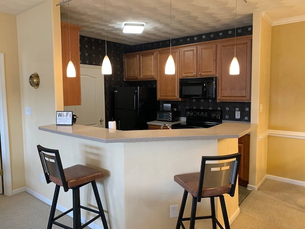 A kitchen with wooden cabinets, a black refrigerator, a microwave, a stove, and two bar stools.