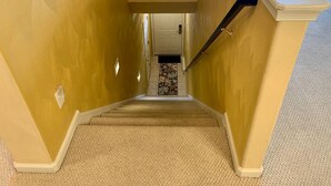 A carpeted staircase leading to a door with a floral rug at the bottom.