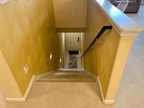 Un escalier recouvert de moquette mène à une porte, et un tapis à motifs floraux se trouve au pied de l’escalier.