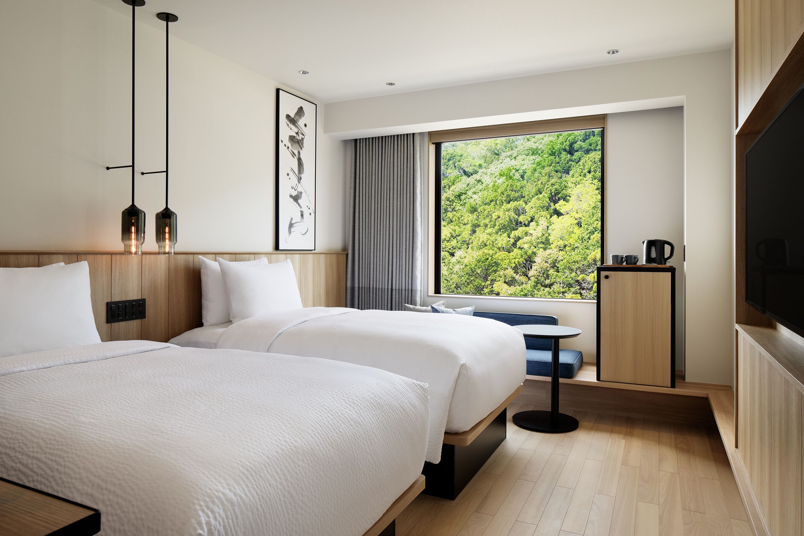 A modern hotel room with two beds, a large window with a forest view, a flat-screen TV, and a small table with a kettle.