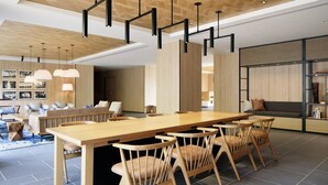 A modern dining area with a wooden table and chairs, pendant lighting, and a sofa in the background. - Fairfield by Marriott Wakayama Kushimoto (Kushimoto)