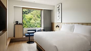 Habitación de hotel moderna con una cama grande, una mesita, un rincón de descanso y una ventana con vistas a zonas verdes.