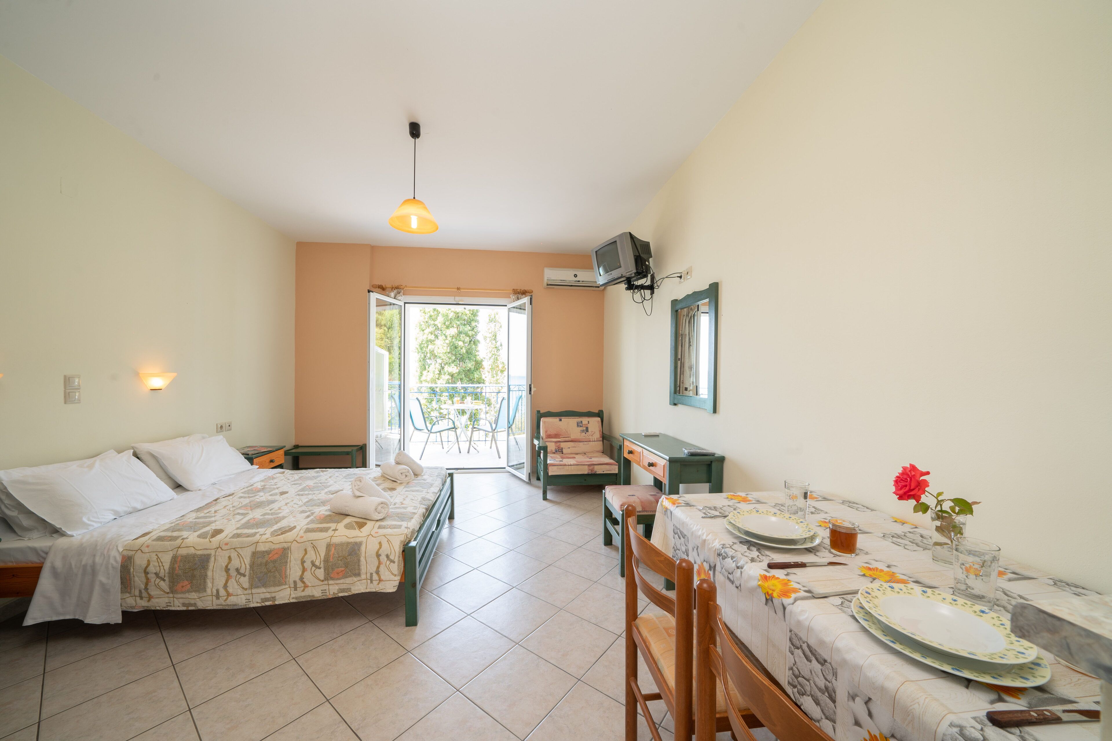A room with a bed, a table set for dining, and a view through an open door.