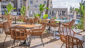 An outdoor patio with wicker furniture, a pool, and a view of a building in the background. - Toxotis Hotel  (Paralimni)