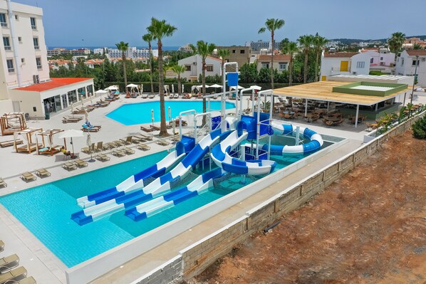 Una piscina con tobogán, sillas de descanso y una zona cubierta con mesas.