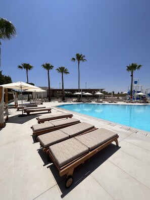 A poolside area with sun loungers, umbrellas, and palm trees.