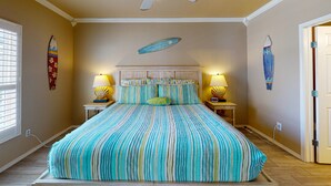 A bedroom with a large bed, striped bedding, two bedside lamps, and a decorative shell wall hanging. - Shared Pool, Near Beach, Pet Friendly (Port Aransas)