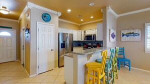 A kitchen with white cabinets, a stainless steel refrigerator, a microwave, and a tiled backsplash. - Shared Pool, Near Beach, Pet Friendly (Port Aransas)