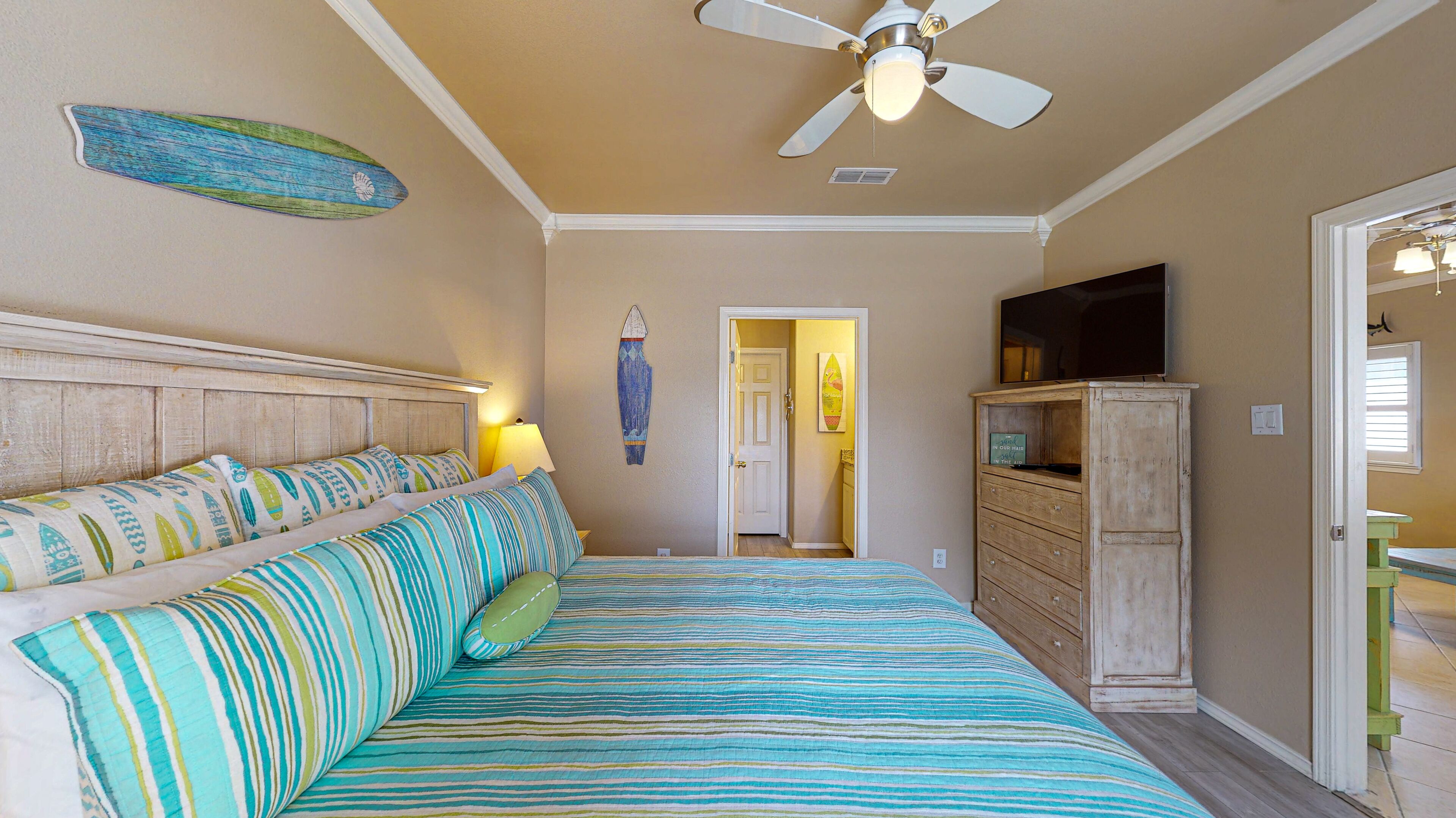 Un dormitorio con cama, ventilador de techo, decoración de tabla de surf, televisor y un mueble de madera.