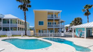 Un área de piscina con dos piscinas, una cerca blanca y un edificio de varios pisos con balcones.