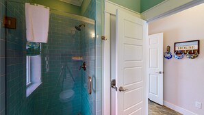 Un baño con ducha de vidrio, una toalla blanca y un estante con artículos de aseo.
