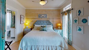 Un dormitorio con cabecera de madera, una cama con edredón blanco, dos mesitas de noche con lámparas y una ventana con cortinas.