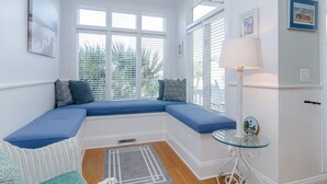 A room with a built-in bench seating area, a small table with a lamp, and a window with blinds.
