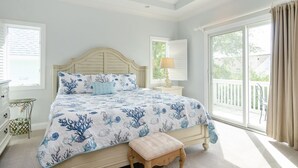 A bedroom with a bed, a nightstand, a lamp, a window, and a view of the outdoors.