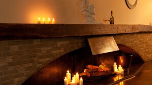A fireplace with lit candles, a statue, and a wine bottle on a mantel.