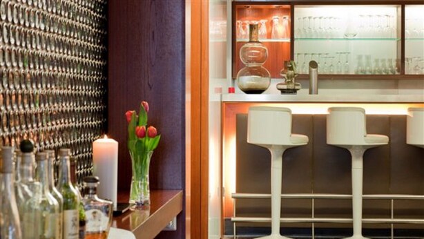 A bar area with stools, a candle, and a display of bottles.