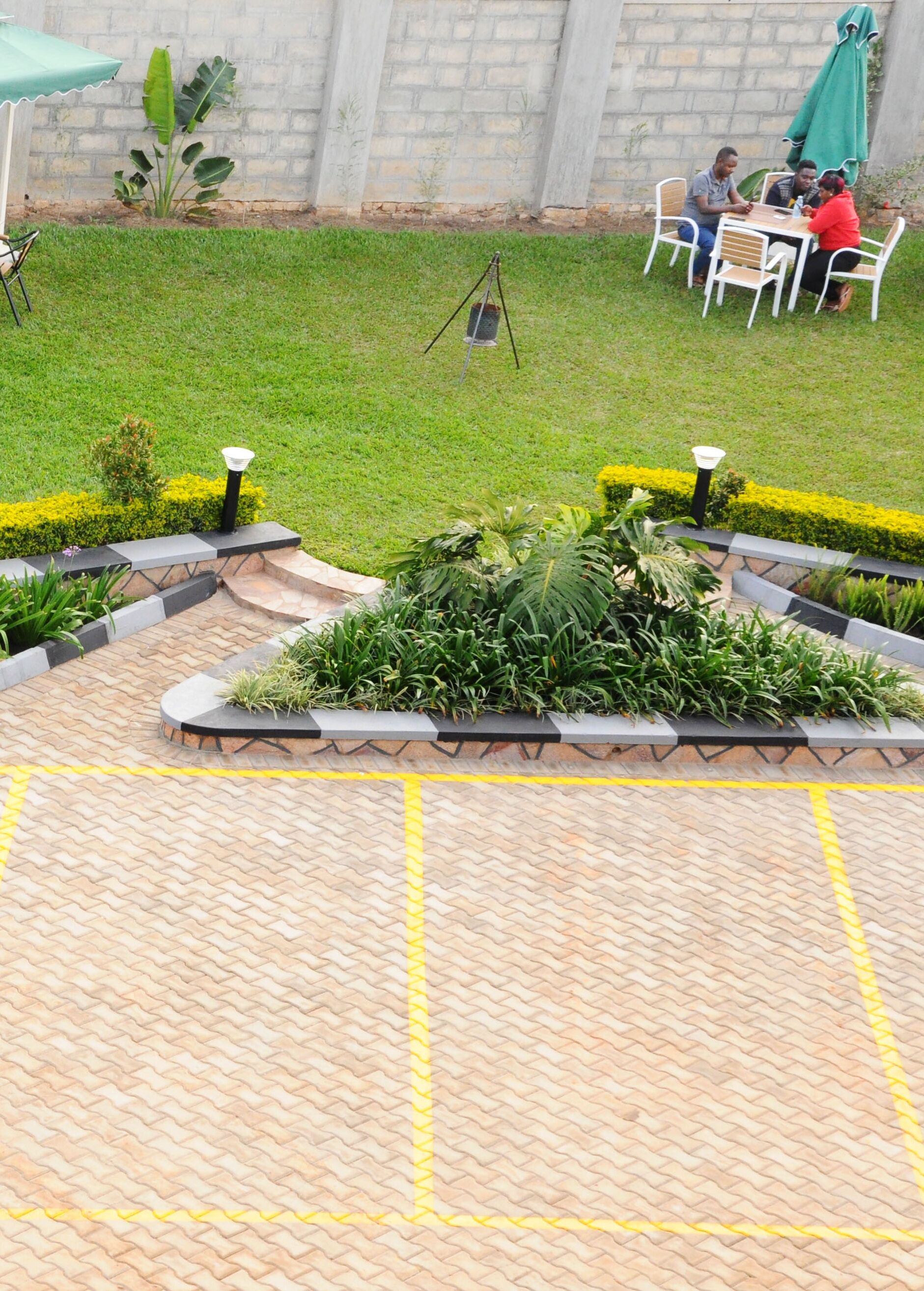 Um espaço de pátio com piso de tijolos, cercado por vegetação bem cuidada e uma parede de tijolos.