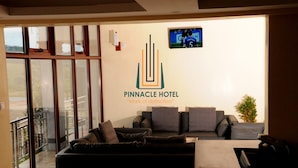 A Pinnacle Hotel reception area with a modern design, featuring a reception desk, a comfortable seating area with a sofa and armchairs, and a large window offering a view of the outdoors. - Pinnacle Hotel Mbarara (Mbarara)