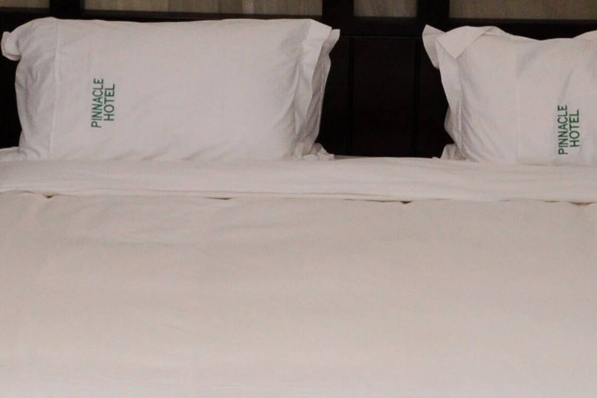 Una cama con ropa de cama y almohadas blancas con la etiqueta "Pinnacle Hotel".