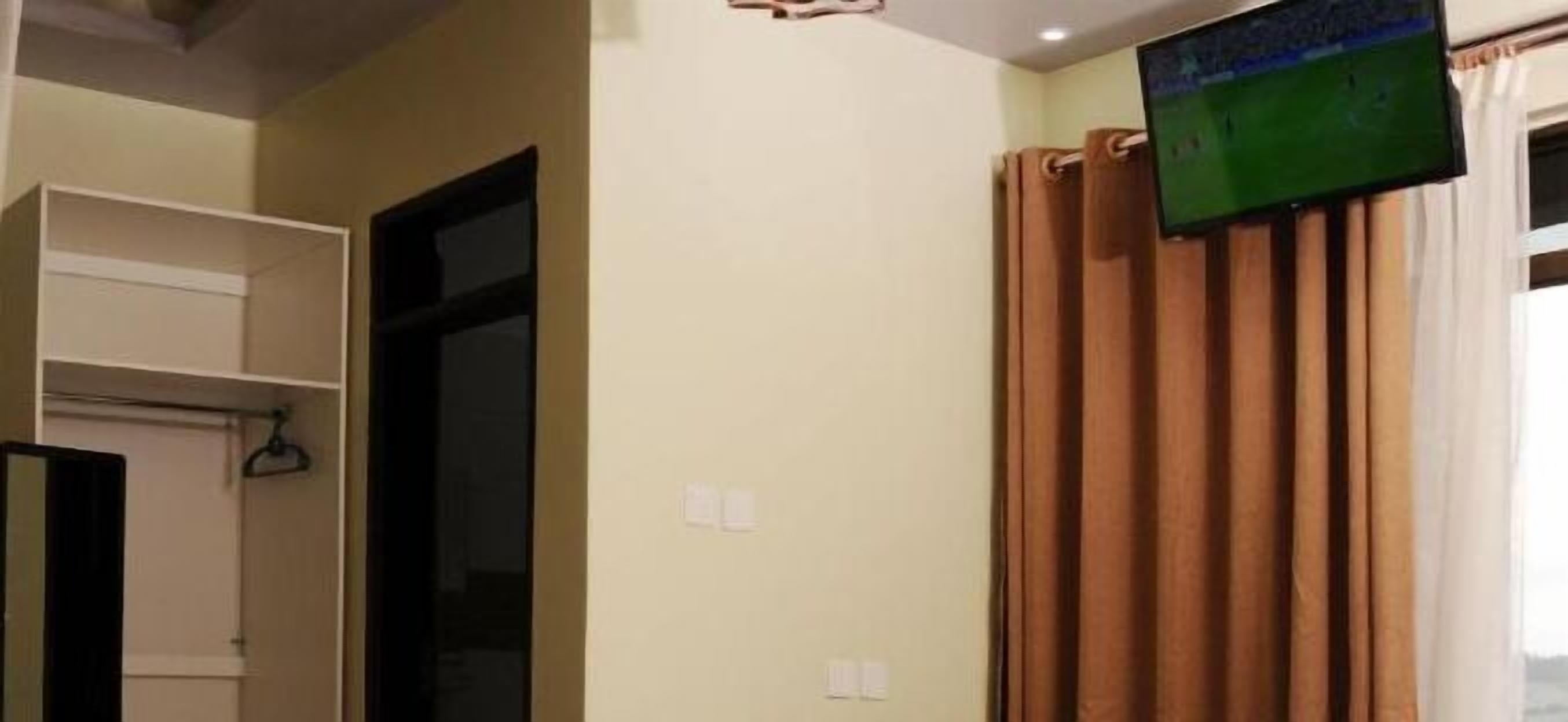 A room with a TV mounted on the wall, a door, and a curtain.