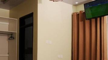 A room with a TV mounted on the wall, a door, and a curtain.