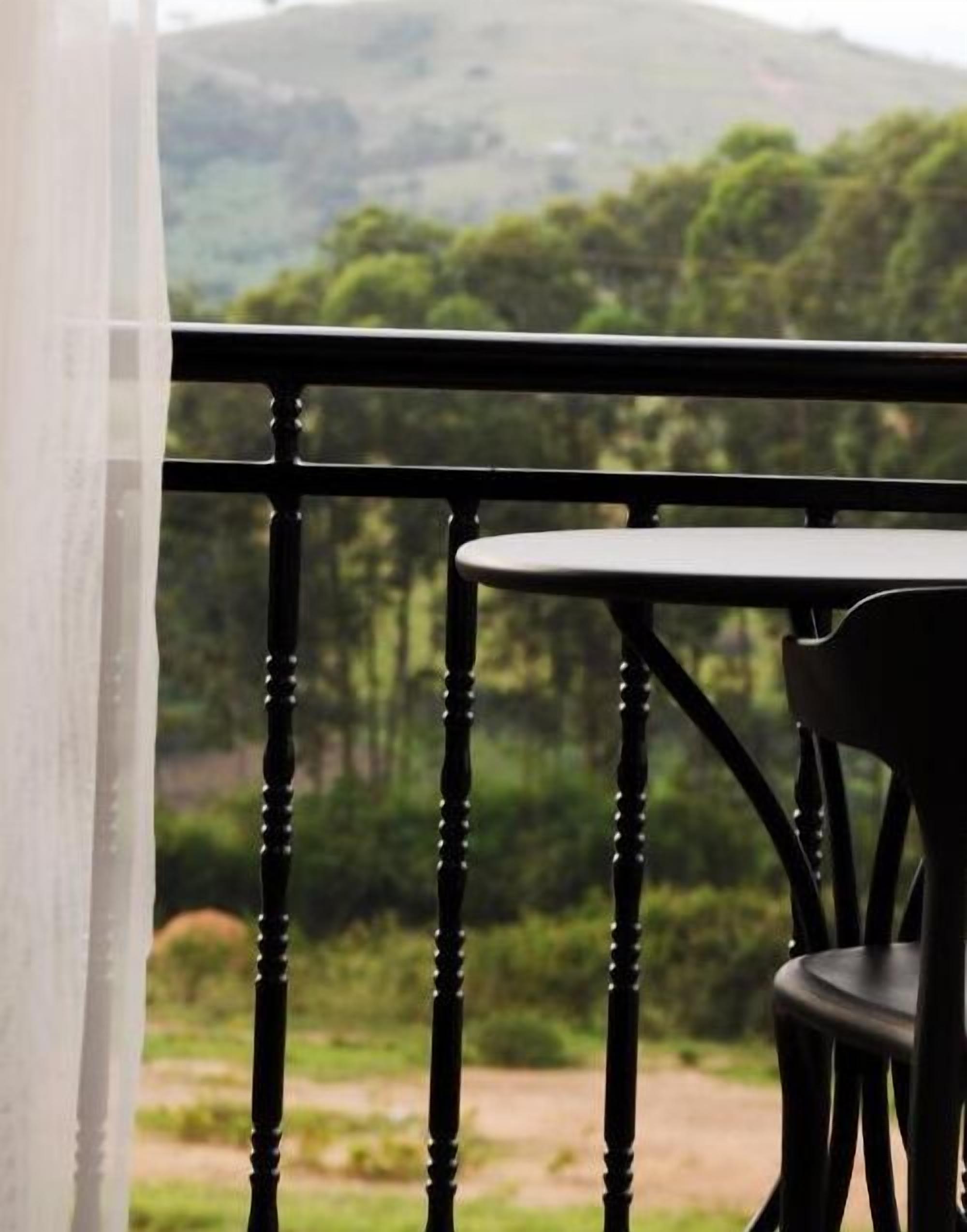 Uma varanda com mesa e cadeira, com vista para uma paisagem verde com árvores e colinas.