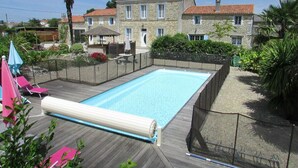 Une piscine rectangulaire dotée d’une terrasse en bois, entourée d’une clôture et d’une végétation luxuriante.