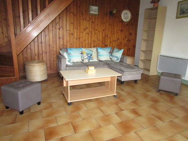 Un salon chaleureux avec un escalier en bois, un canapé d’angle gris agrémenté de coussins décoratifs, une petite table basse en bois et un panier en osier.