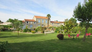 Un jardin bien entretenu, avec un bâtiment en pierre en arrière-plan, et une terrasse agrémentée de chaises.