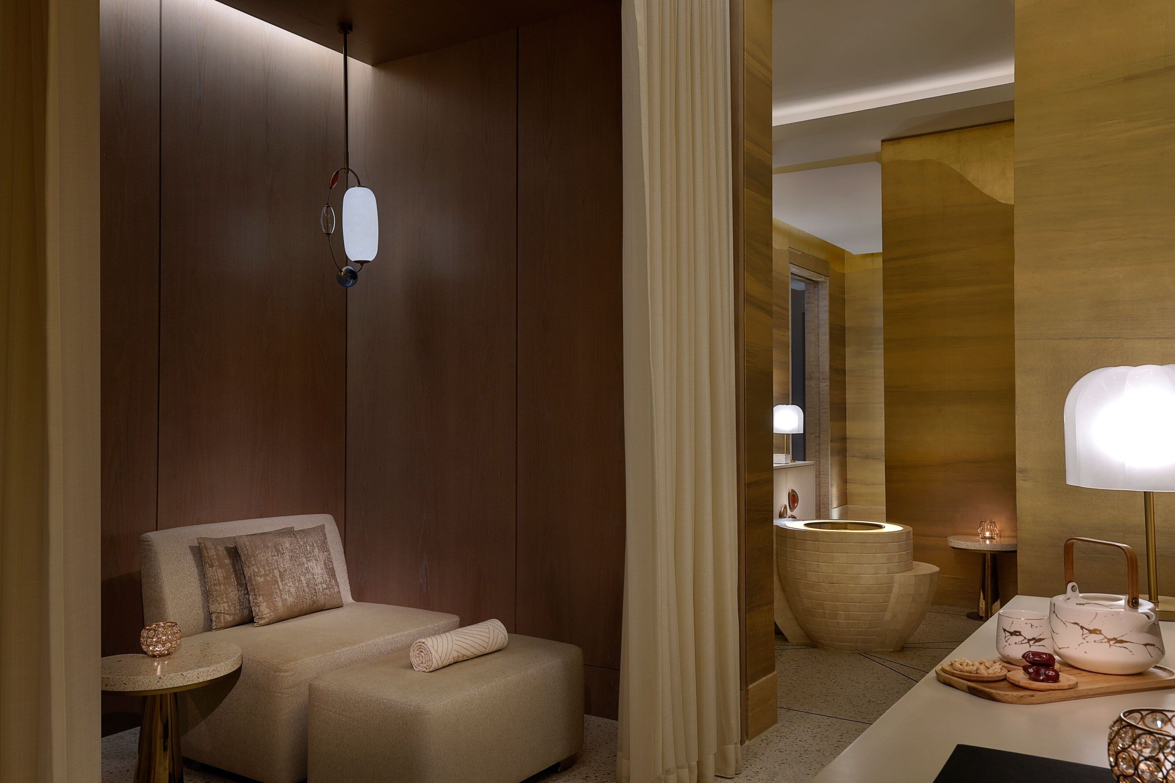 Una habitación de hotel moderna con un sofá, una mesita, un espejo y una mesita de noche con lámpara.