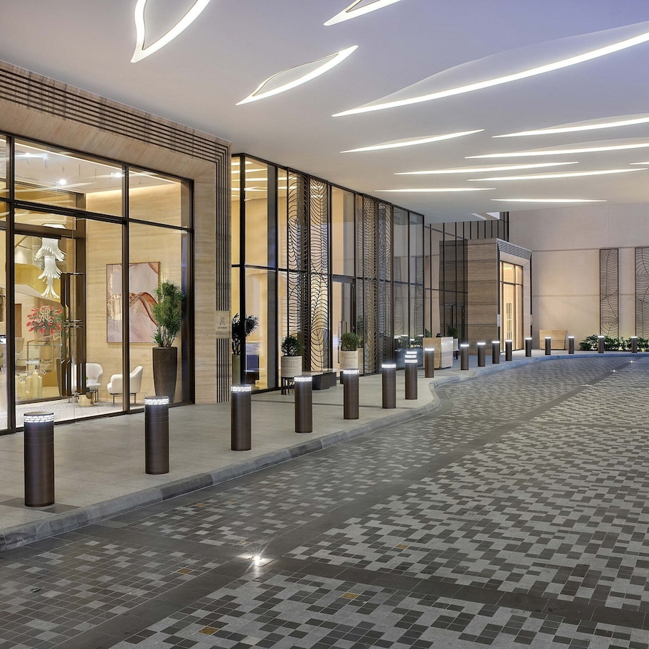 A modern hotel lobby with a tiled floor, glass doors, and a series of bollards.