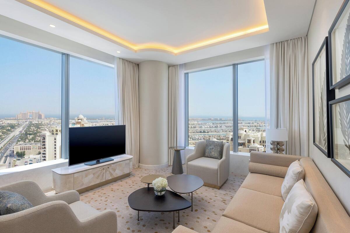 A modern living room with a large flat-screen TV, comfortable seating, and a city view.