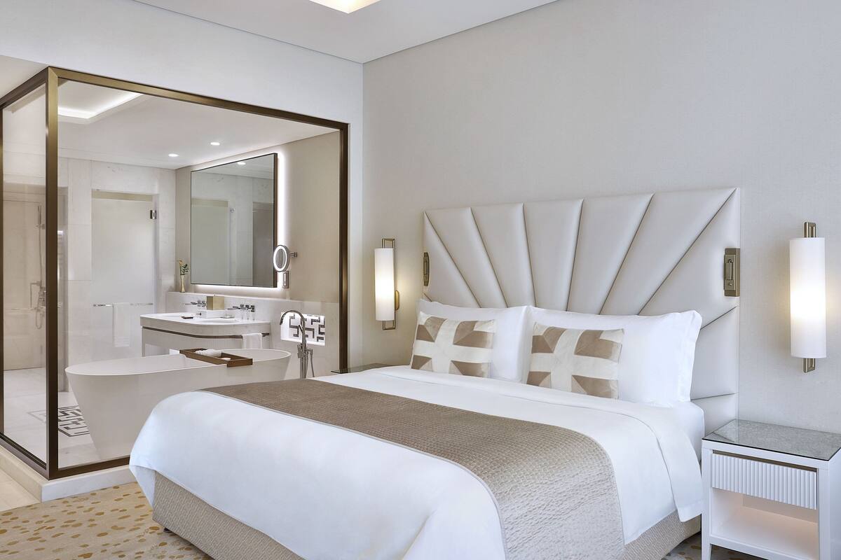 A modern hotel room with a large bed, a separate bathroom with a glass shower enclosure, and a small bedside table.