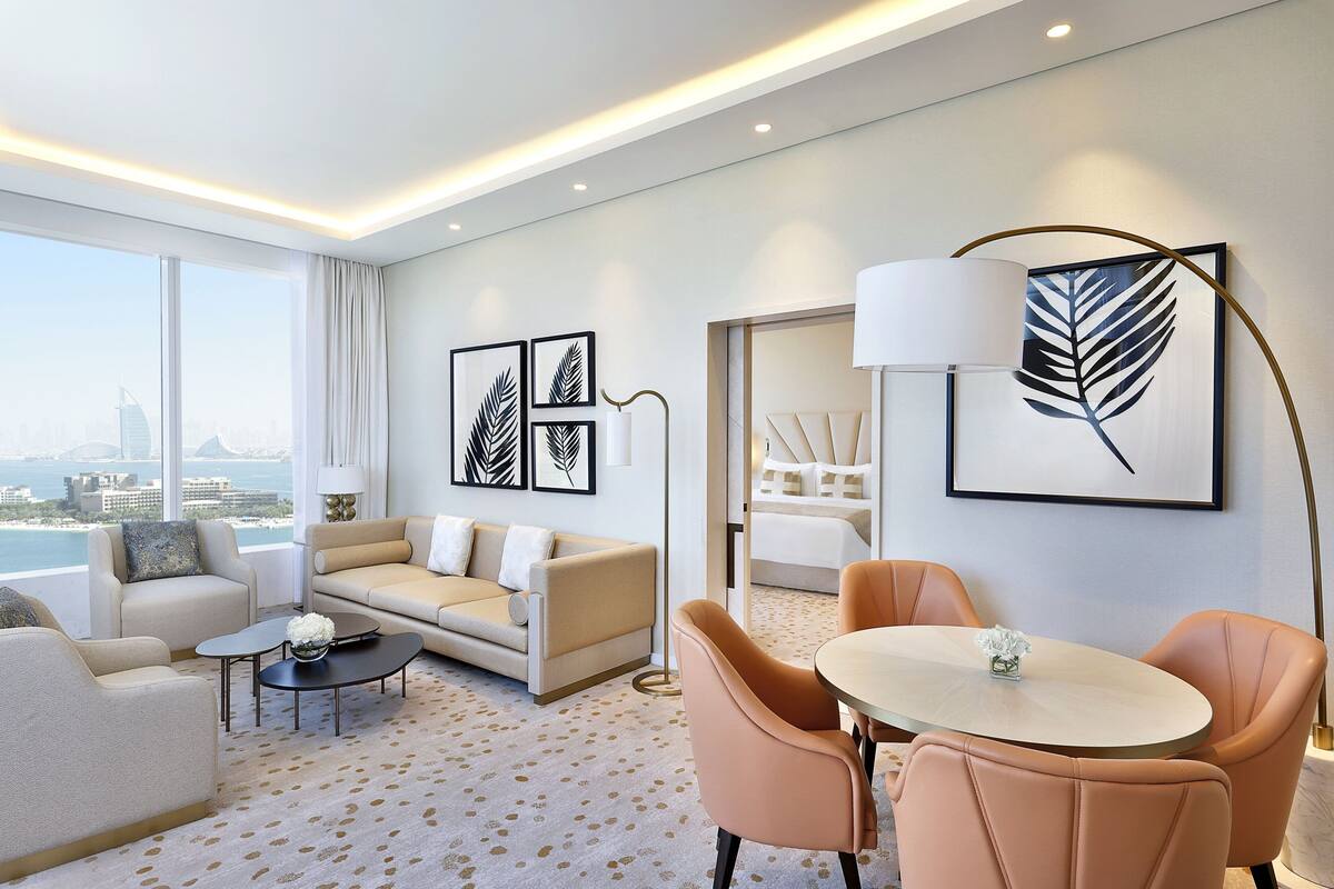 A modern hotel room with a sofa, chairs, a round table, and artwork on the walls.