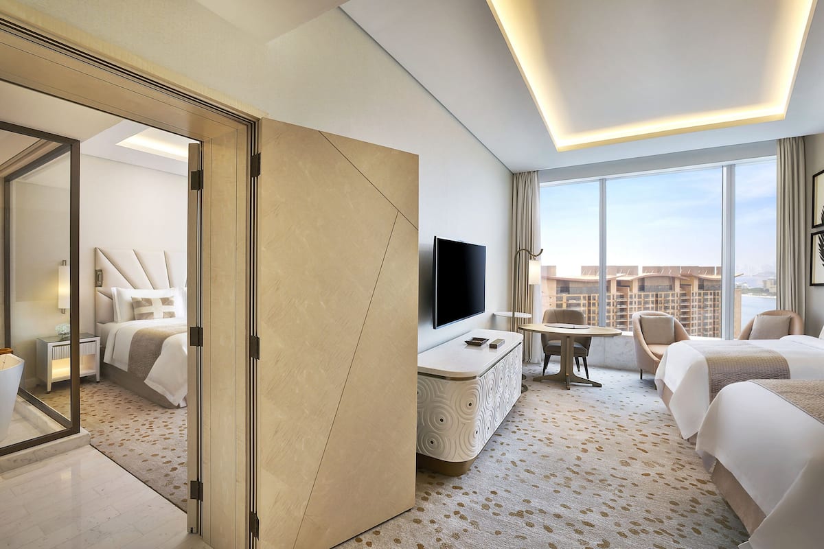 A modern hotel room with a large bed, a TV, a desk, and a view of the city.