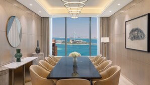 A modern dining room with a large table, comfortable chairs, a vase with flowers, and a view of a cityscape and water. - The St. Regis Dubai, The Palm (Dubai)