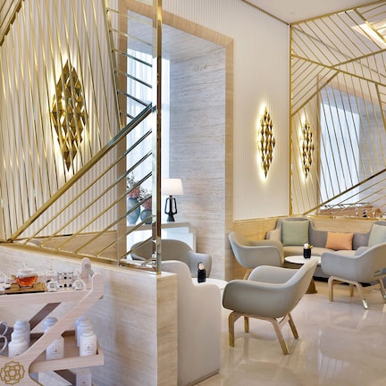 A modern hotel lobby with a central staircase, seating area, and a display of tea sets.