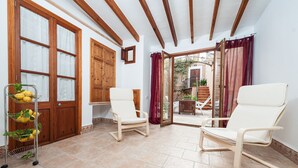 A room with two white chairs, a metal fruit cart, wooden doors, and a view of an outdoor area with a staircase. - Ca Na Blanca (Alcúdia)